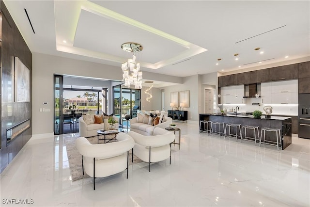 living room with a tray ceiling, a chandelier, and sink