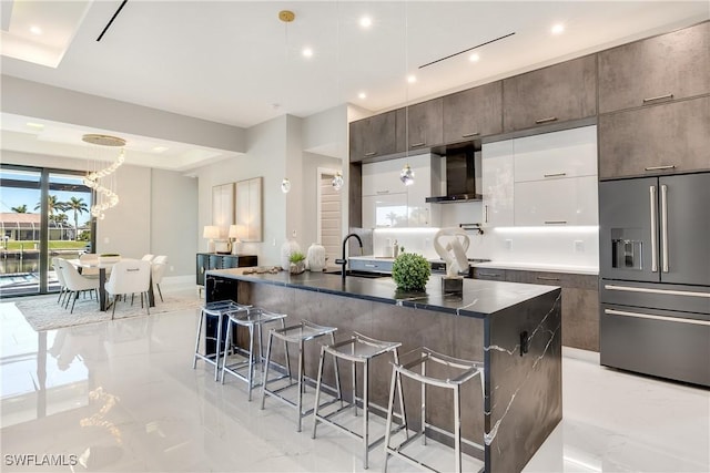 kitchen with a breakfast bar, sink, high end refrigerator, a kitchen island with sink, and wall chimney range hood