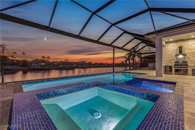 pool at dusk with a lanai, a patio, a water view, an in ground hot tub, and exterior kitchen