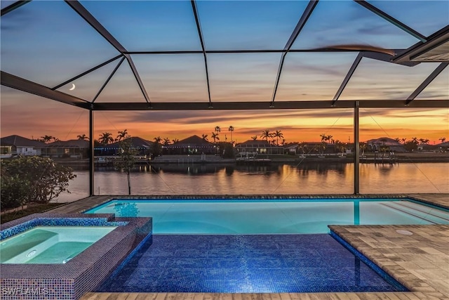 pool at dusk with an in ground hot tub, a water view, a lanai, and a patio area