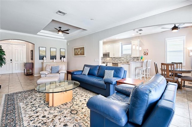 living area featuring light tile patterned floors, visible vents, arched walkways, and ornamental molding