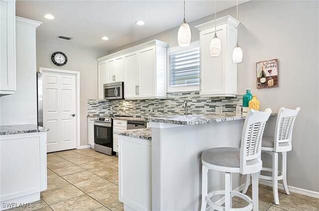 kitchen with pendant lighting, appliances with stainless steel finishes, white cabinetry, light stone countertops, and a kitchen bar