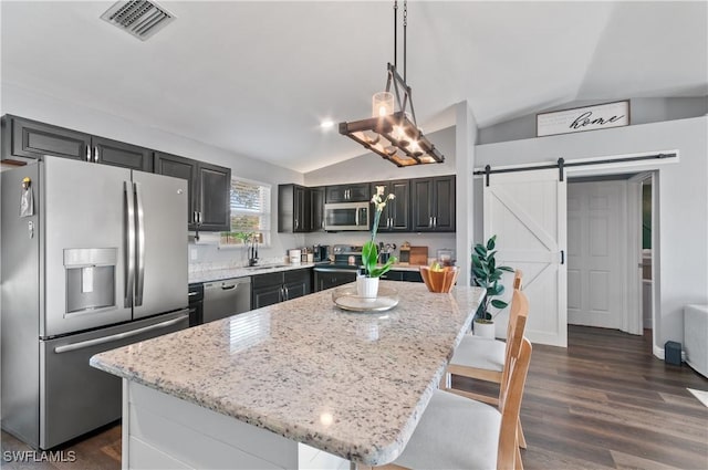 kitchen featuring light stone counters, decorative light fixtures, a center island, appliances with stainless steel finishes, and a barn door