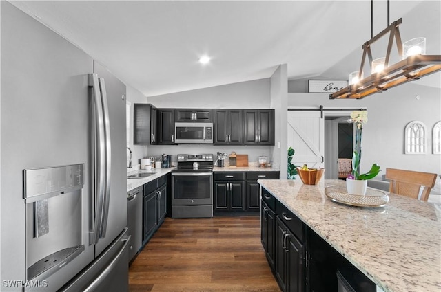 kitchen with appliances with stainless steel finishes, dark hardwood / wood-style floors, hanging light fixtures, light stone countertops, and a barn door