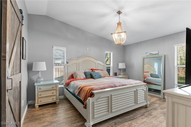 bedroom with an inviting chandelier, hardwood / wood-style flooring, vaulted ceiling, and a barn door