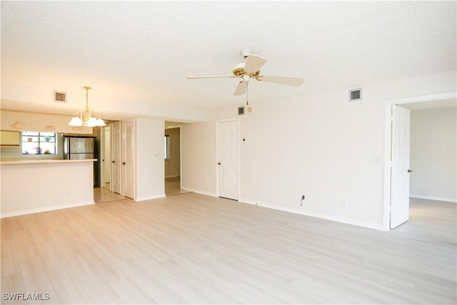 unfurnished living room with ceiling fan with notable chandelier, a textured ceiling, and light wood-type flooring