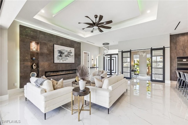 living room featuring a raised ceiling, a tile fireplace, a barn door, and ceiling fan