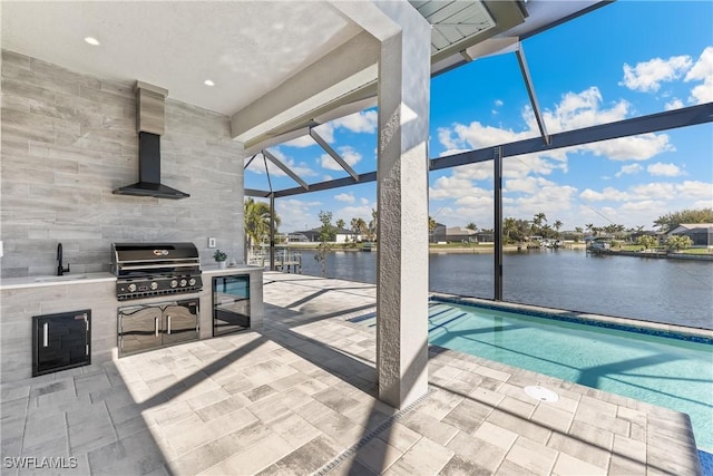 view of patio / terrace featuring an outdoor kitchen, a grill, sink, glass enclosure, and a water view