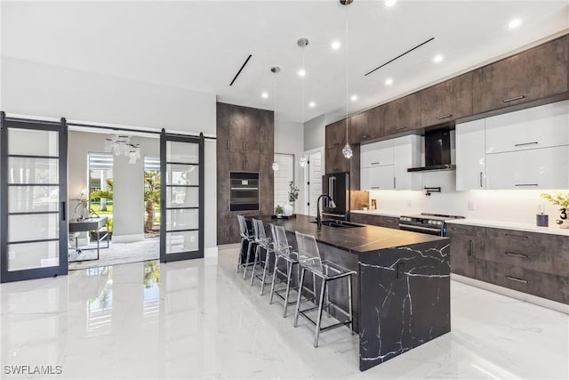 kitchen featuring white cabinetry, a kitchen island with sink, stainless steel appliances, a barn door, and wall chimney range hood