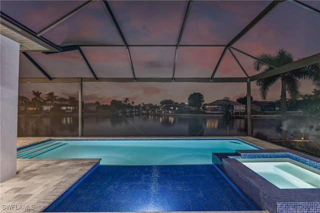 pool at dusk with an in ground hot tub, a water view, a lanai, and a patio