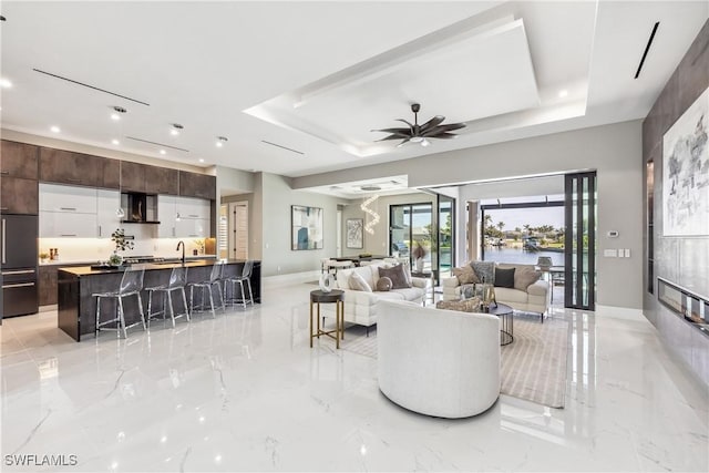 living room with ceiling fan, a tray ceiling, and sink