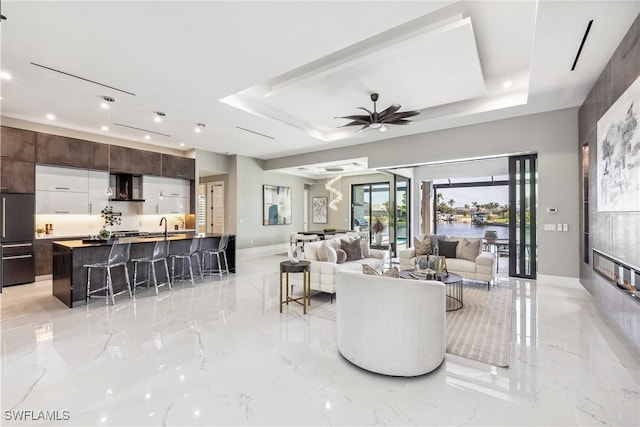 living room with sink, ceiling fan, and a tray ceiling