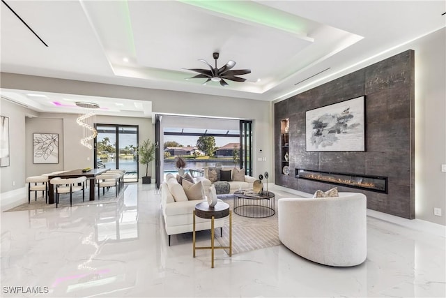 living room featuring a tiled fireplace, a raised ceiling, and ceiling fan