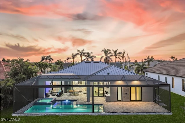 back house at dusk with a pool with hot tub, a lawn, glass enclosure, and a patio area