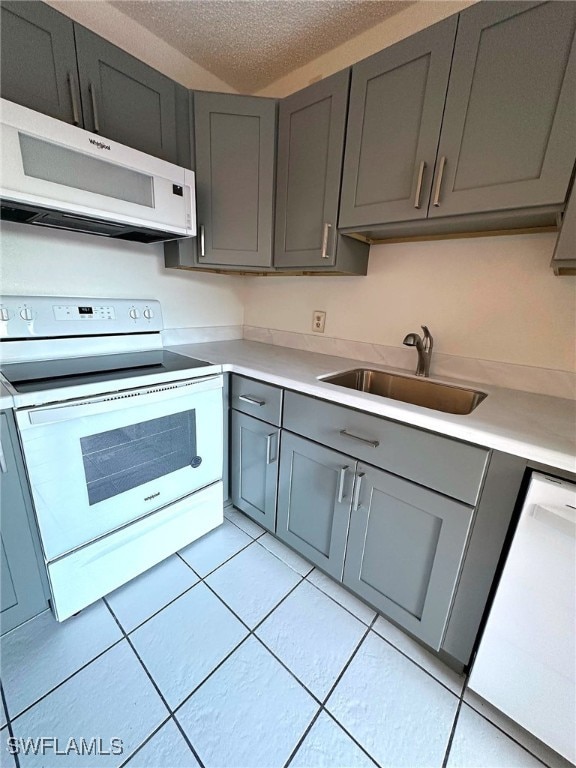 kitchen with sink, a textured ceiling, light tile patterned floors, gray cabinets, and white appliances