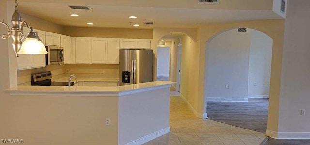 kitchen featuring light tile patterned floors, stainless steel appliances, kitchen peninsula, and white cabinets