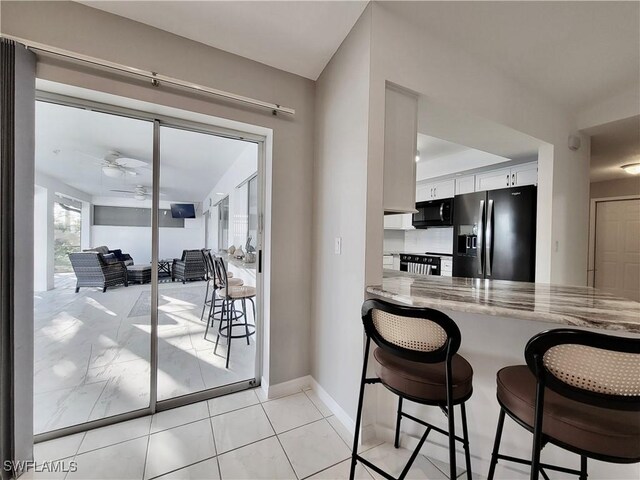 kitchen with a breakfast bar area, white cabinets, ceiling fan, light stone counters, and stainless steel refrigerator with ice dispenser