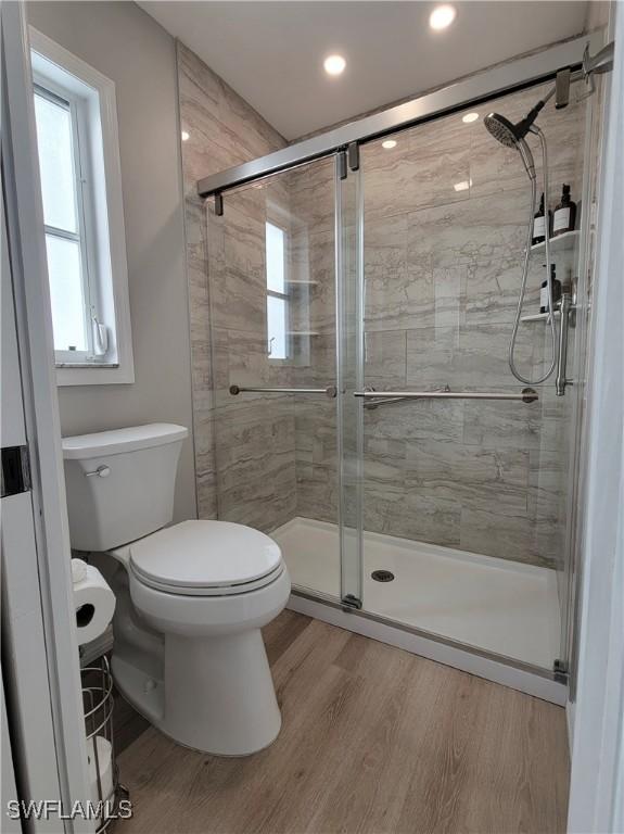 bathroom featuring hardwood / wood-style floors, plenty of natural light, a shower with door, and toilet