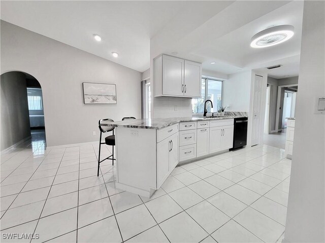 kitchen with white cabinetry, black dishwasher, a kitchen breakfast bar, kitchen peninsula, and light stone countertops