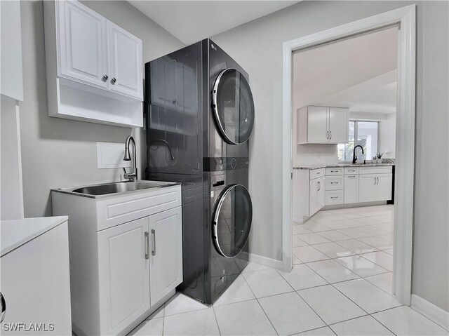 laundry area with cabinets, stacked washer / drying machine, sink, and light tile patterned floors