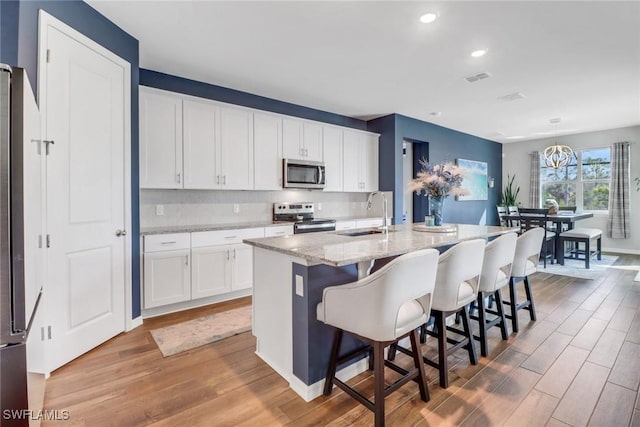 kitchen featuring sink, white cabinetry, a center island with sink, appliances with stainless steel finishes, and a kitchen breakfast bar