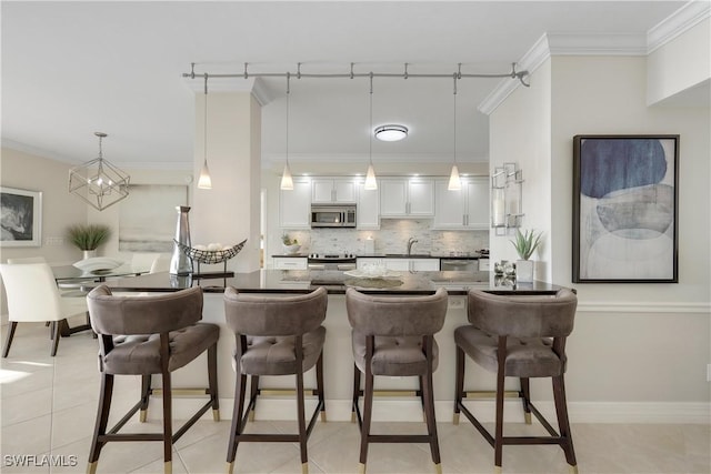 interior space with a kitchen bar, tasteful backsplash, pendant lighting, stainless steel appliances, and white cabinets