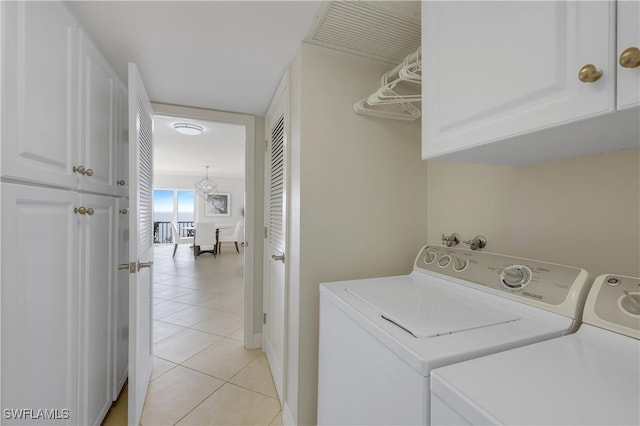 clothes washing area with separate washer and dryer, light tile patterned floors, and cabinets