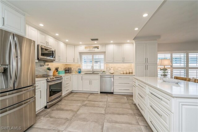 kitchen with tasteful backsplash, appliances with stainless steel finishes, sink, and white cabinets