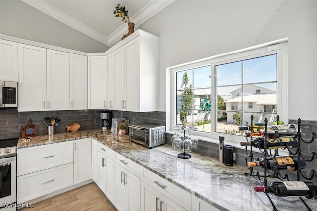 kitchen featuring white cabinetry, appliances with stainless steel finishes, crown molding, and light stone counters