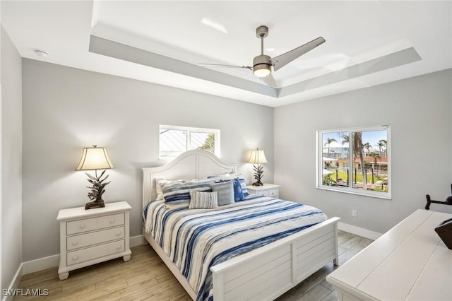 bedroom featuring a tray ceiling, multiple windows, and light wood-type flooring