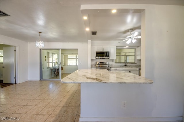 kitchen with stainless steel appliances, light stone counters, white cabinets, light tile patterned flooring, and decorative light fixtures