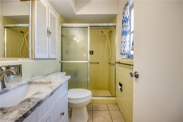 bathroom featuring tile patterned floors, toilet, tile walls, vanity, and a shower with door