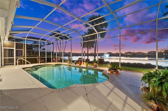 pool at dusk with a patio area, a water view, and glass enclosure