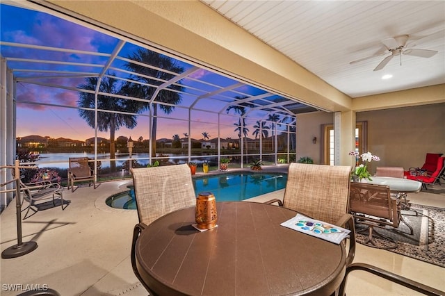 pool at dusk with a patio, a water view, ceiling fan, and a lanai