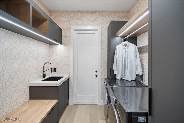 clothes washing area with cabinets, sink, light hardwood / wood-style floors, and washing machine and dryer