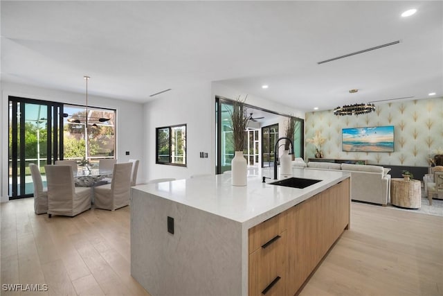 kitchen with sink, hanging light fixtures, a large island, a notable chandelier, and light hardwood / wood-style flooring