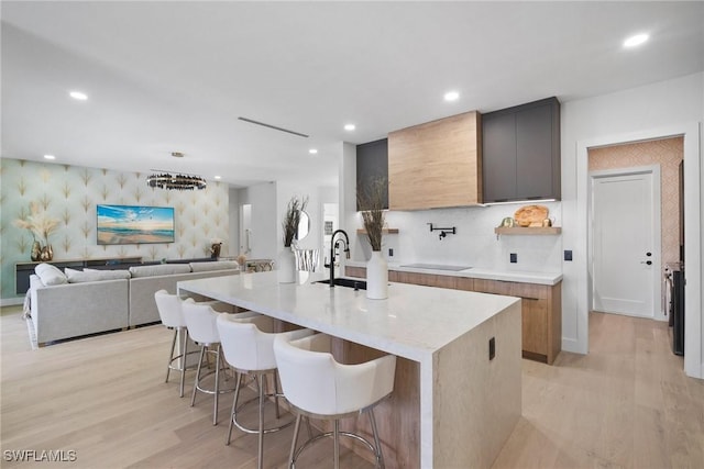 kitchen with sink, an island with sink, a breakfast bar area, and light hardwood / wood-style flooring