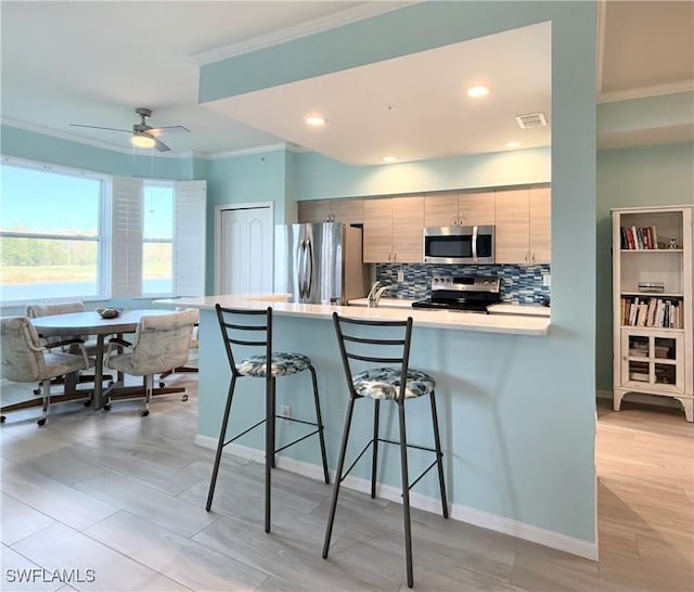 kitchen with a kitchen bar, crown molding, appliances with stainless steel finishes, kitchen peninsula, and decorative backsplash