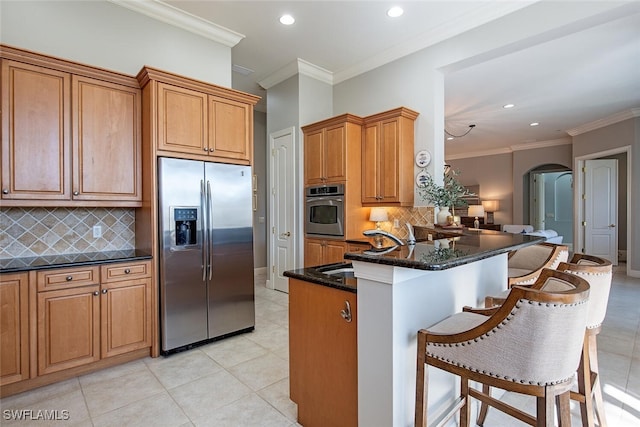 kitchen with appliances with stainless steel finishes, dark stone countertops, a kitchen breakfast bar, ornamental molding, and kitchen peninsula