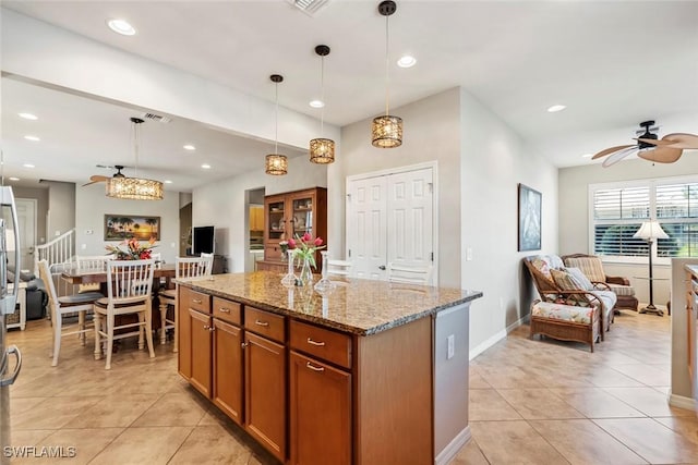 kitchen with light stone counters, a kitchen island, hanging light fixtures, and light tile patterned floors