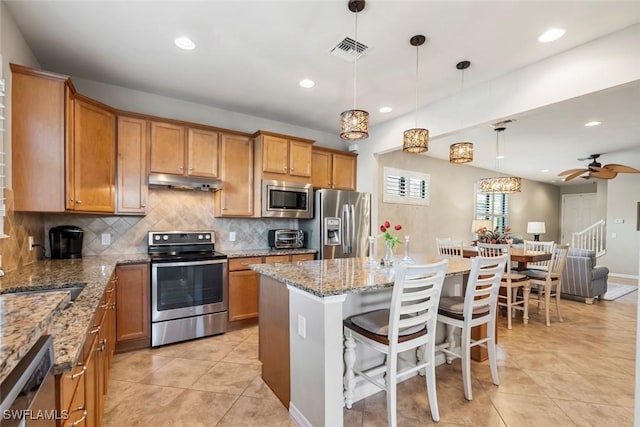 kitchen with pendant lighting, a breakfast bar, stainless steel appliances, a center island, and light stone countertops