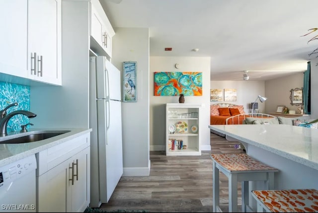 kitchen with sink, white appliances, dark wood-type flooring, white cabinetry, and light stone counters