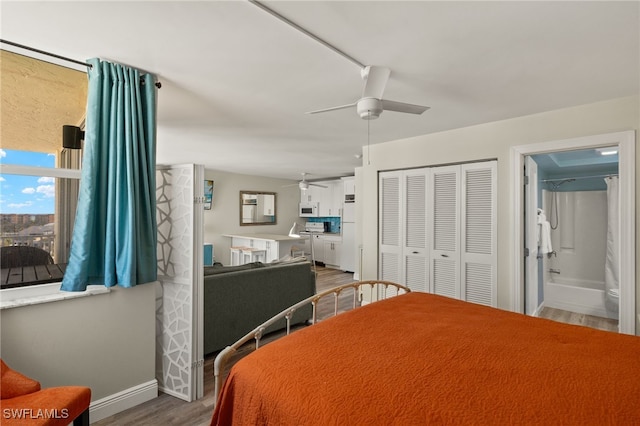 bedroom featuring ceiling fan, wood finished floors, baseboards, a closet, and ensuite bath