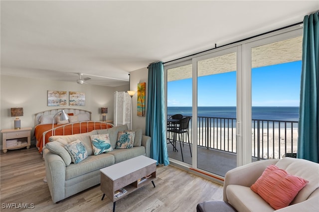 bedroom with a water view, light hardwood / wood-style flooring, a view of the beach, access to outside, and a wall of windows