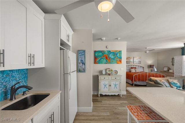 kitchen featuring light wood-style floors, freestanding refrigerator, white cabinetry, a sink, and ceiling fan