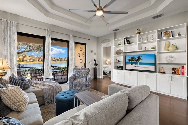 living room with arched walkways, dark wood-type flooring, a water view, visible vents, and a tray ceiling