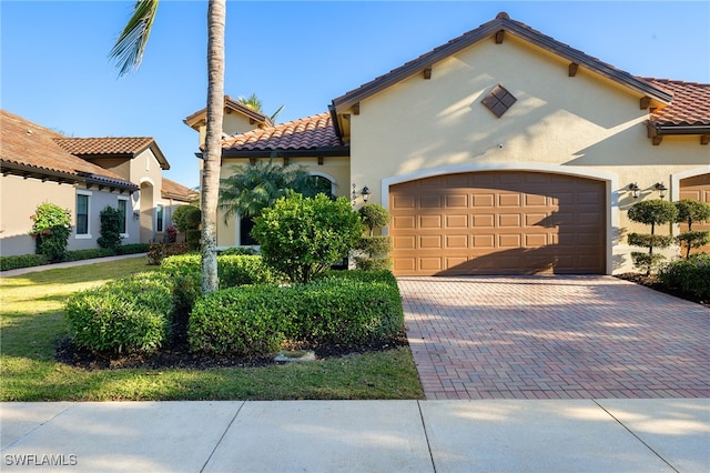 mediterranean / spanish home with a garage, a tiled roof, decorative driveway, and stucco siding