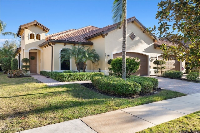 mediterranean / spanish-style home featuring an attached garage, a tile roof, driveway, stucco siding, and a front yard