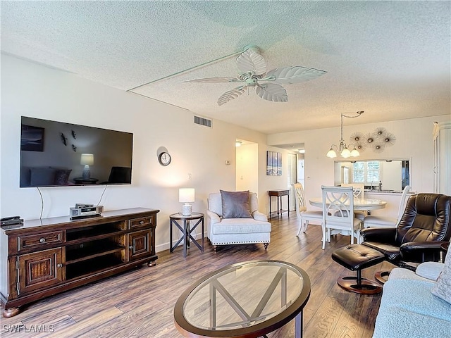 living room featuring ceiling fan with notable chandelier, light hardwood / wood-style floors, and a textured ceiling