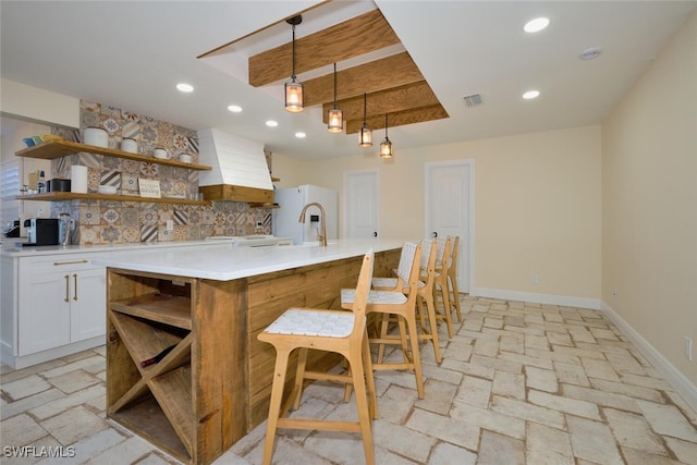 kitchen featuring a kitchen bar, white cabinetry, hanging light fixtures, custom range hood, and a kitchen island with sink